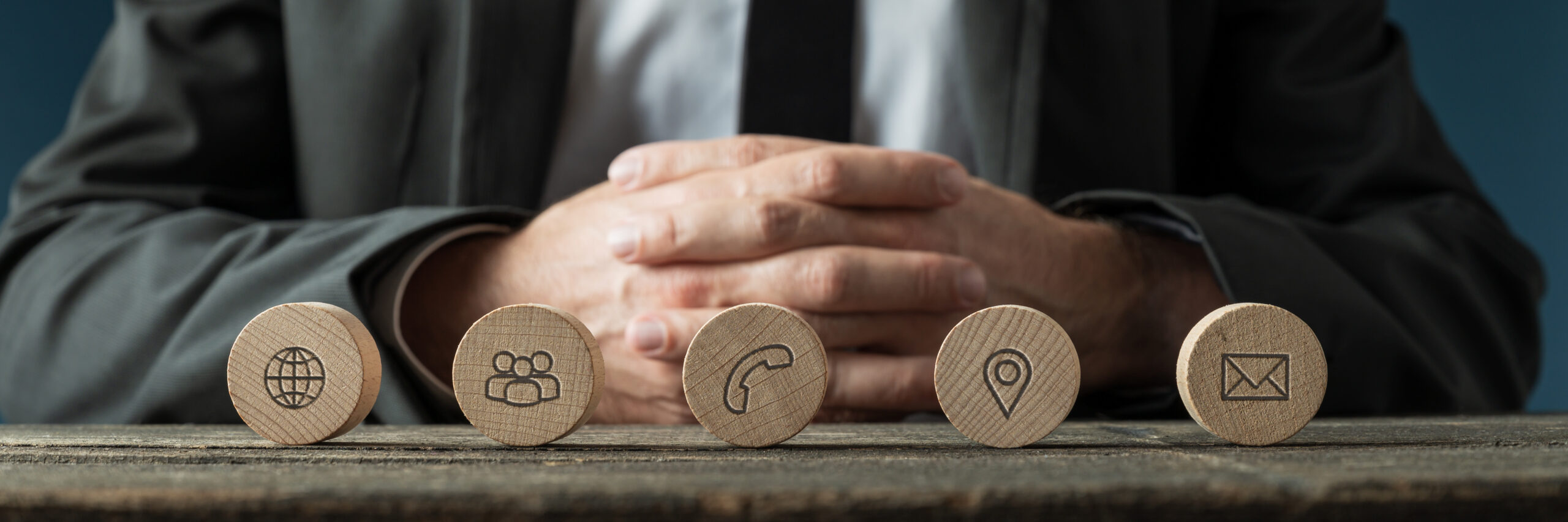 Wide view image of business customer service representative sitting at a desk with a line of wooden cut circles with contact and information icons on them in front of him.